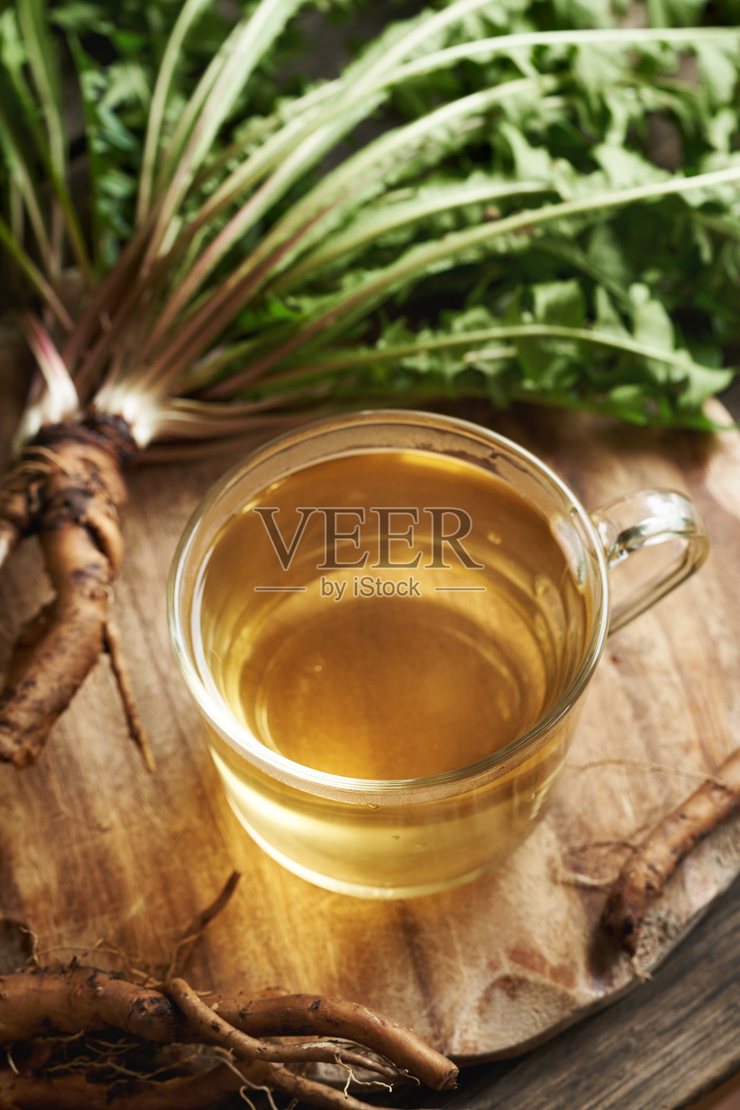 一杯草药茶，配有新鲜的蒲公英根和叶子，放在木桌上照片摄影图片