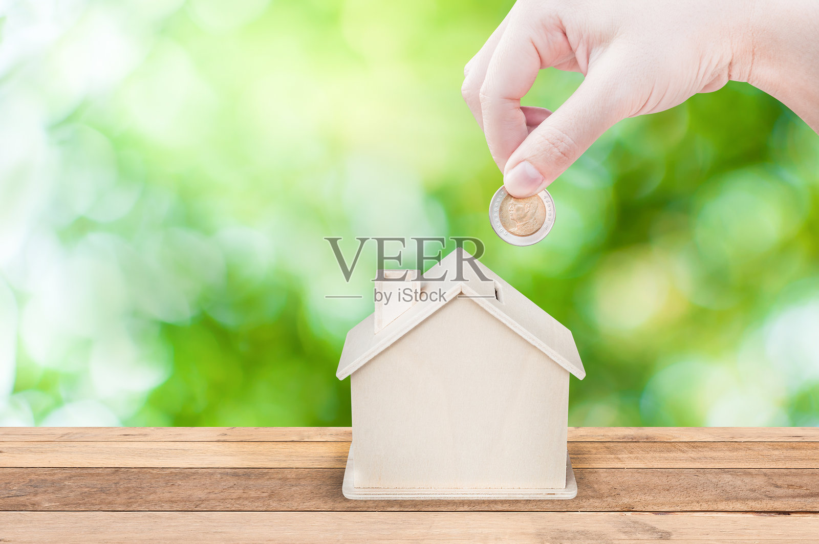 特写镜头：一个人将硬币放入木制房子中照片摄影图片