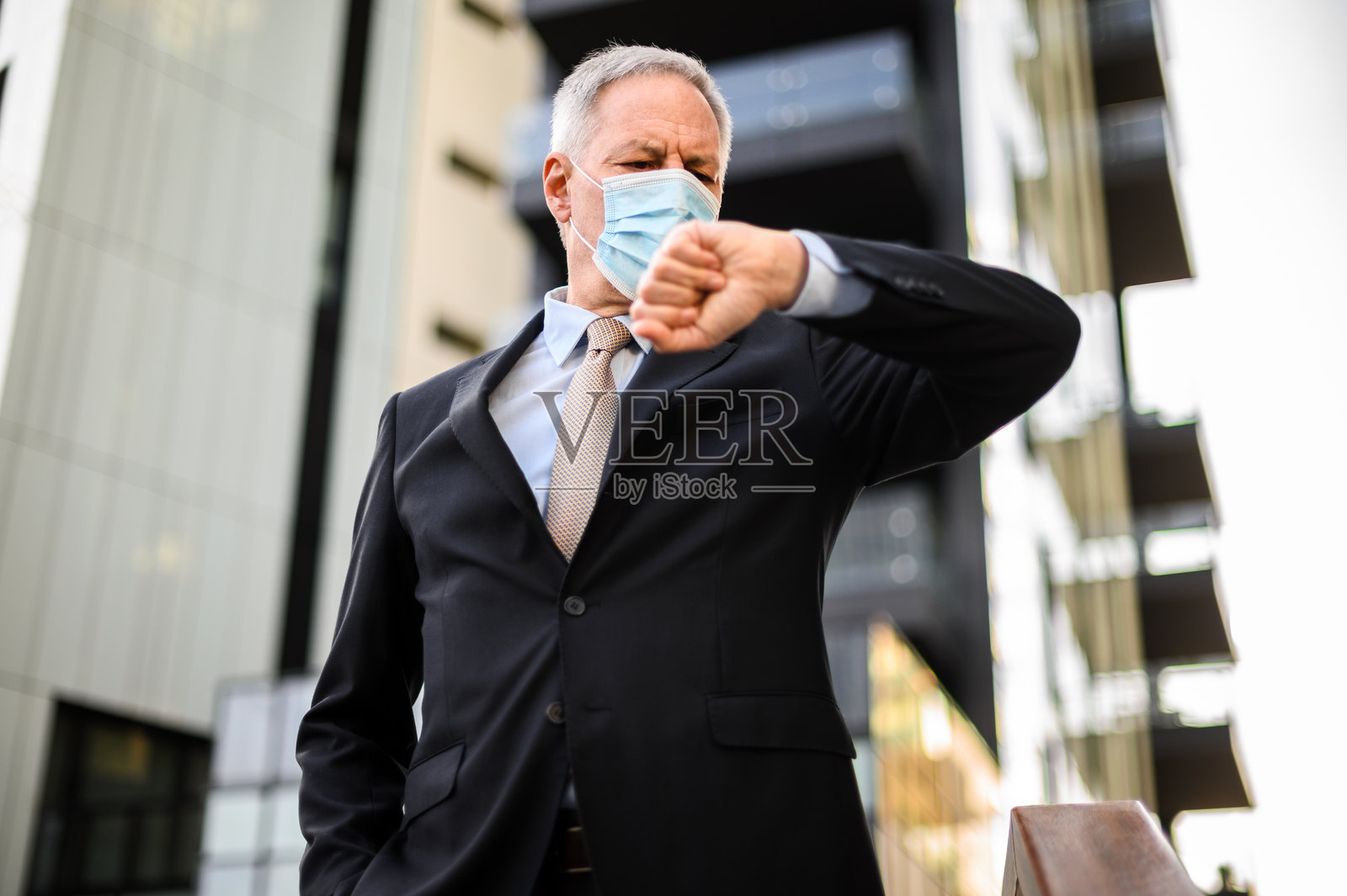 商人在户外戴着防护口罩查看手腕上的手表时间照片摄影图片