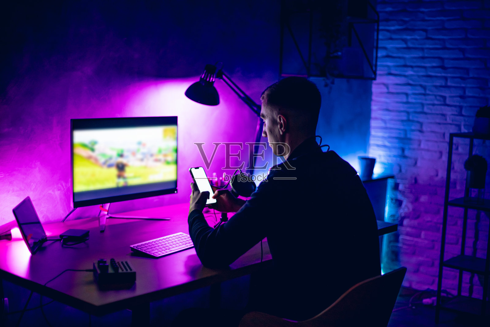 年轻男子在霓虹灯照明的房间里玩游戏时使用手机照片摄影图片