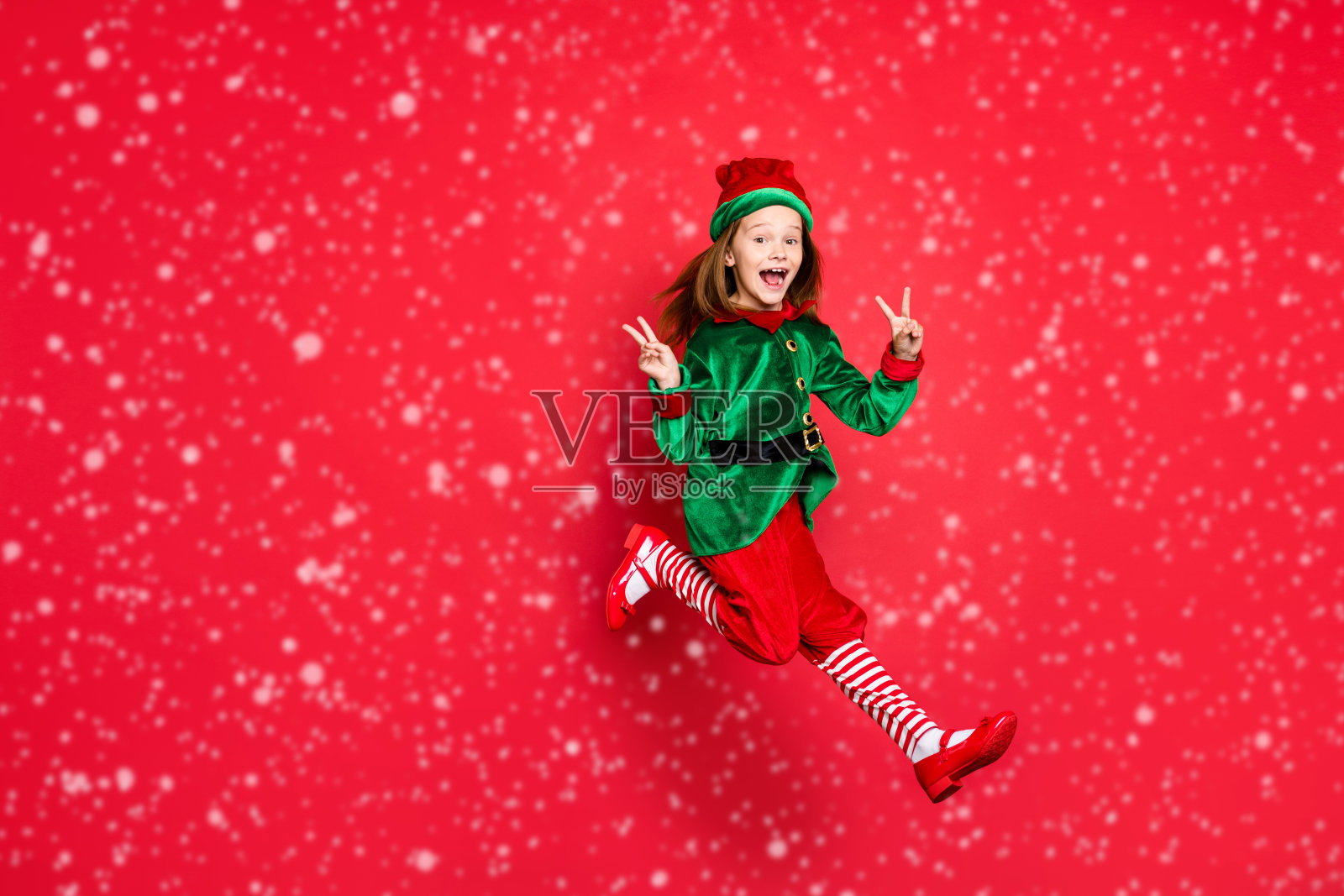 全身身材的可爱乐观小精灵在明亮鲜艳的红色背景下开心地做出V字手势，充满乐趣。照片摄影图片