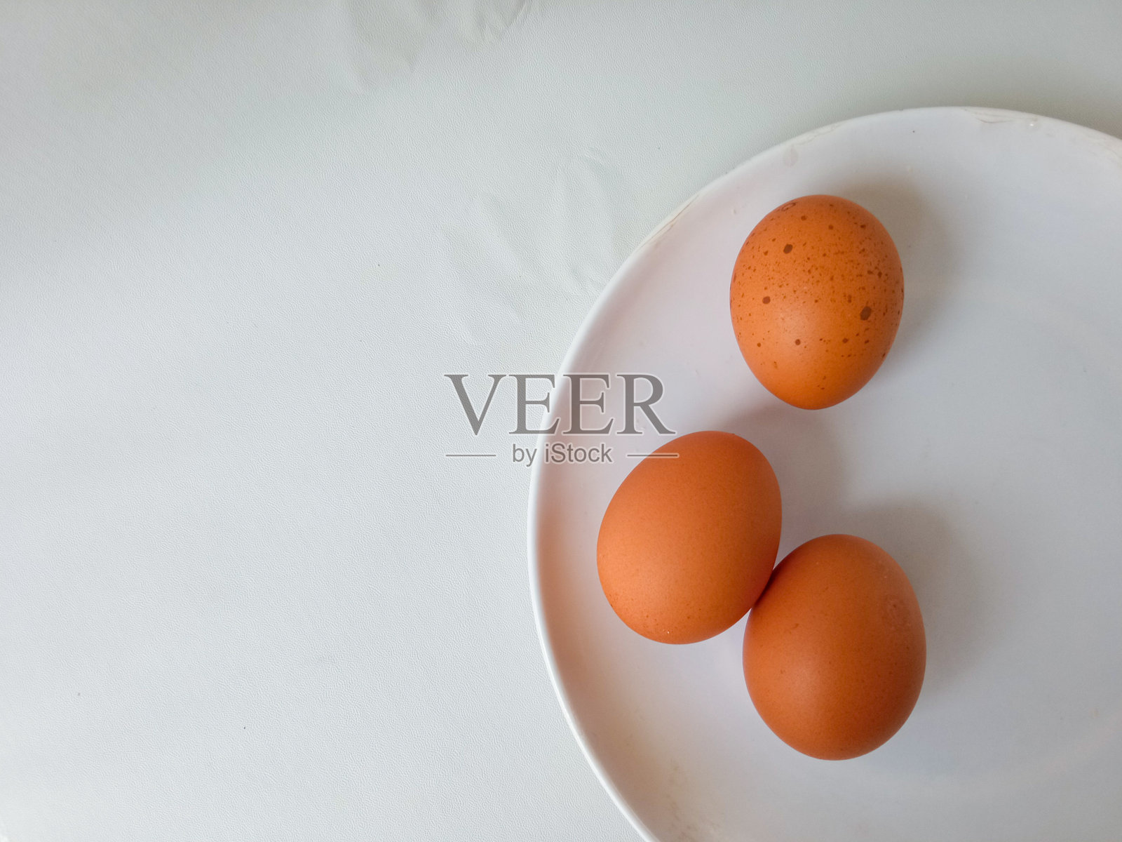 三只鸡蛋放在白色盘子里，背景为白色。照片摄影图片