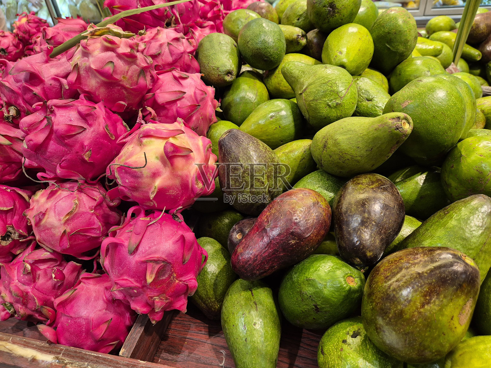 一堆新鲜采摘的红心火龙果和鳄梨在市场上展示。照片摄影图片