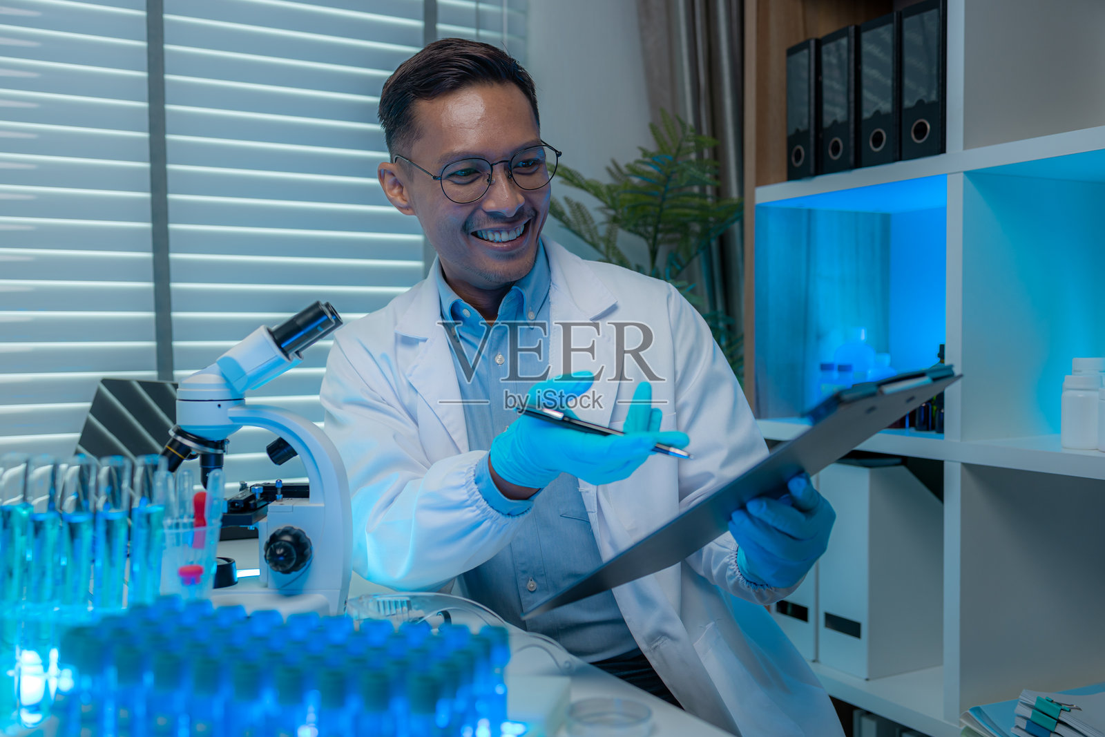 一位科学家和他的助手在实验室里一起工作，周围有许多科学设备，如显微镜、试管、烧杯和移液管，两位科学家在工作场所内。照片摄影图片