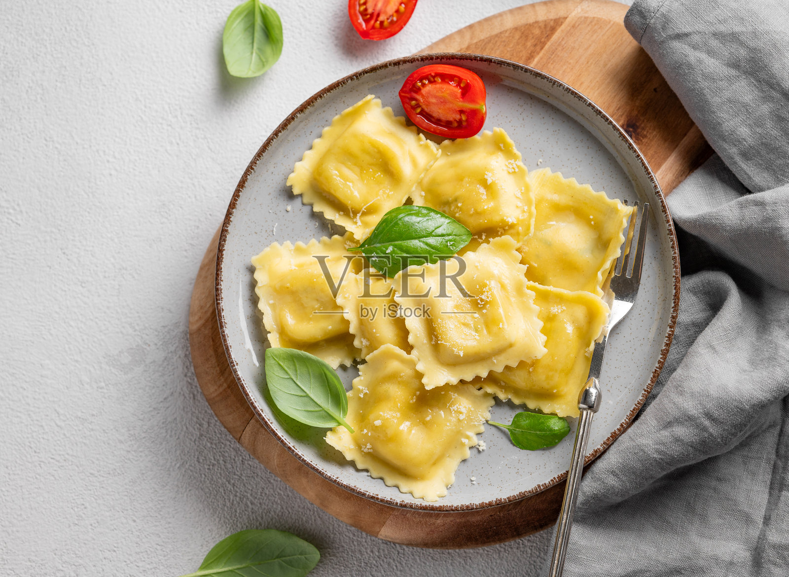 自制的意大利饺子，里面夹着奶酪、番茄和罗勒，放在木板上的盘子里，背景为浅色。照片摄影图片