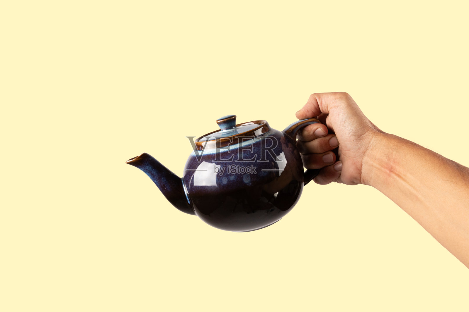 男性手握着一个蓝色陶瓷茶壶，背景为黄色。照片摄影图片