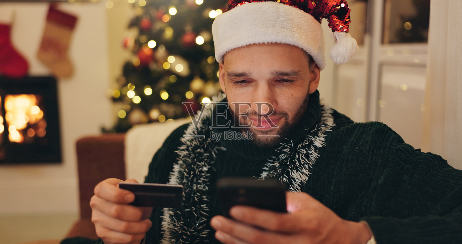 圣诞节，手持信用卡的男人进行在线购物，数字购买或礼物订单。节日季节，假期和在家使用智能手机进行银行应用、互联网支付或电子商务的人。照片摄影图片