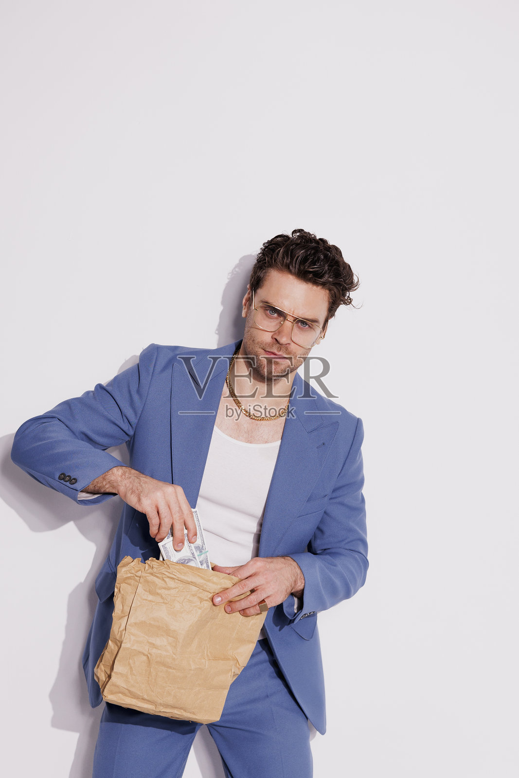 自信时尚的富人将美元放入纸袋中，背景为灰色。照片摄影图片