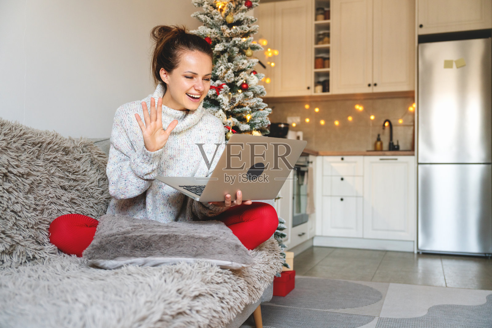 女人在家里的沙发上舒适地坐着，利用笔记本电脑进行视频通话，享受圣诞假期。照片摄影图片