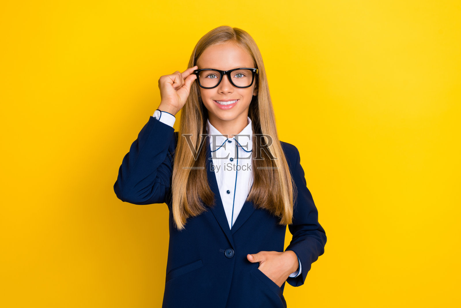 一位积极可爱的小女孩，手臂触碰眼镜，佩戴新配饰，欢欣鼓舞，穿着时尚衣服，背景为黄色。照片摄影图片