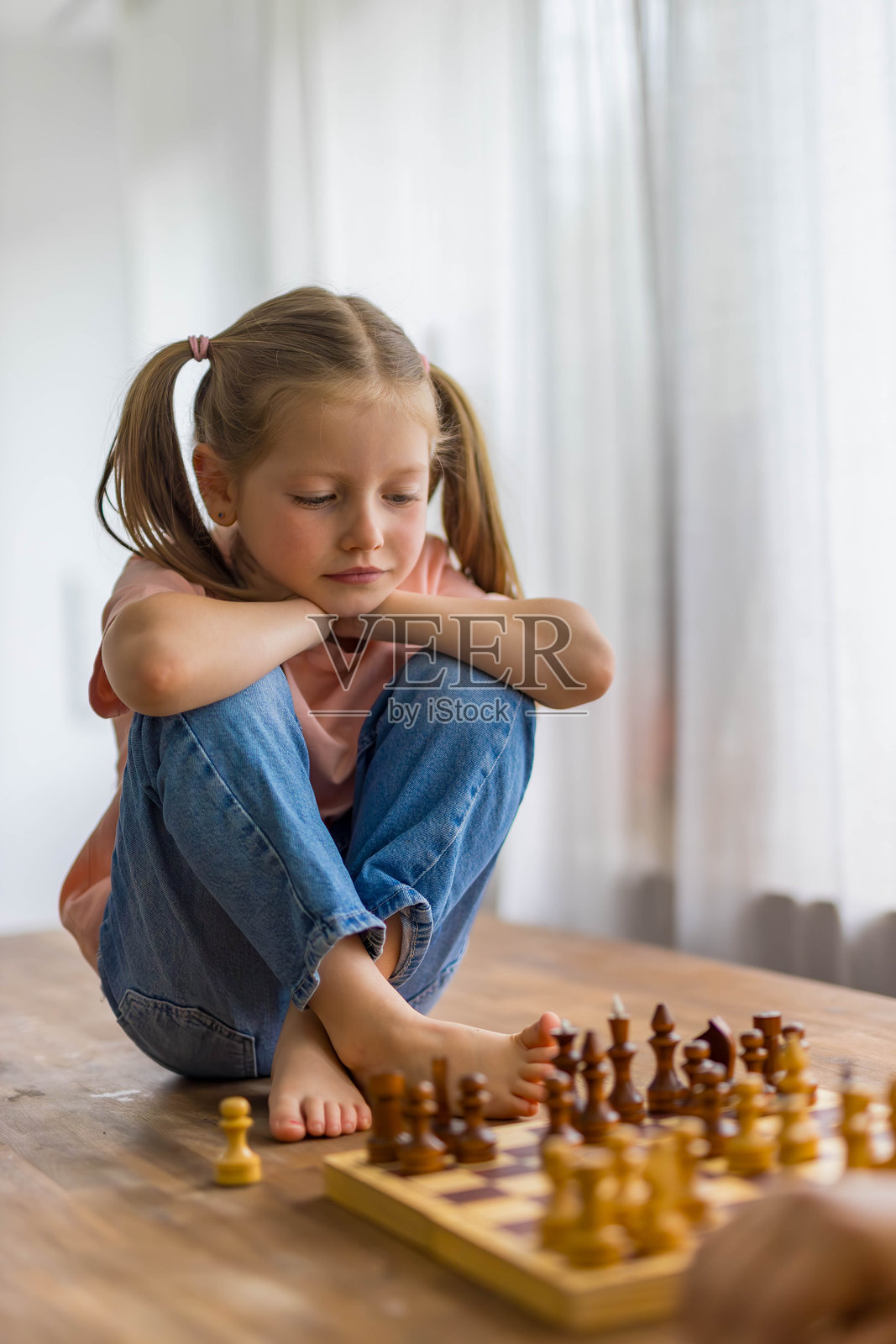 5岁女孩在玩迷你国际象棋，专注地仔细计划她的下一步棋。照片摄影图片