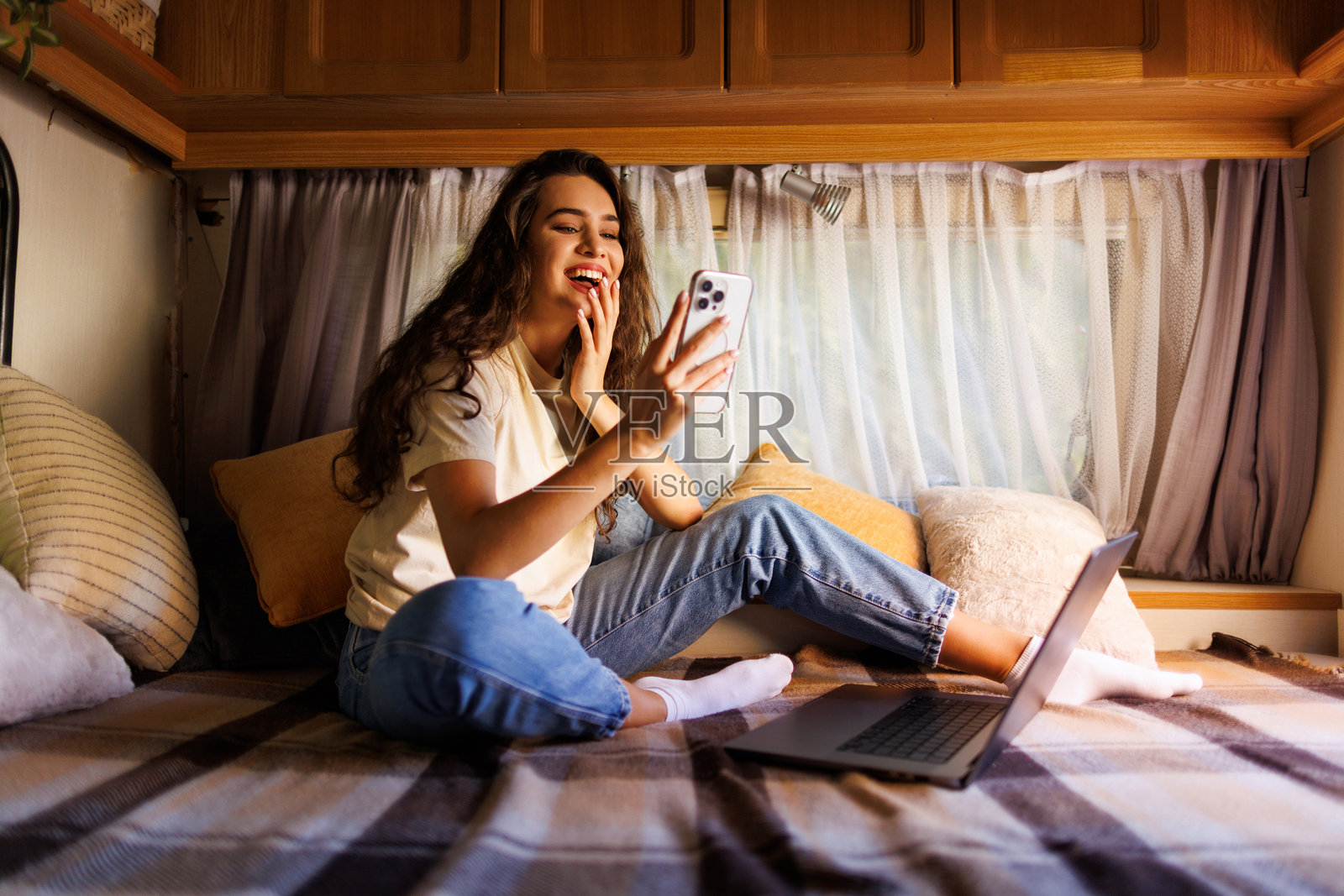 年轻女性在拖车旁用手机在笔记本电脑前工作。照片摄影图片