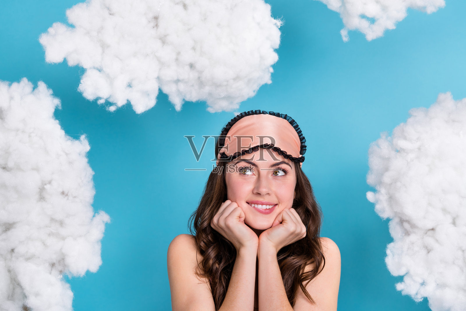 一位迷人、开朗的波浪卷发女孩在明亮的蓝色背景下思考飞翔的云朵。照片摄影图片