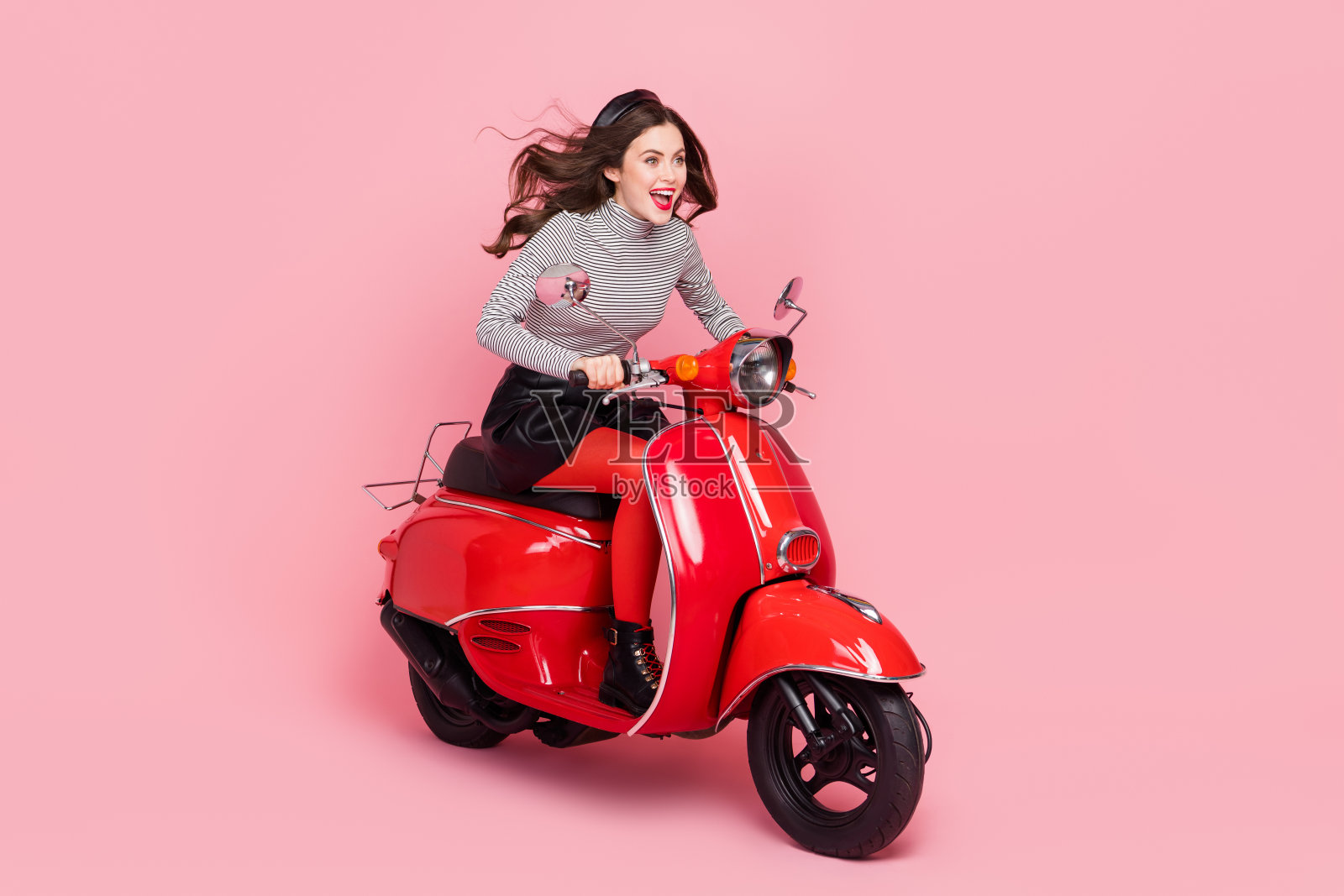 兴奋的时尚潮流女士骑着极限摩托车，穿着紧身裤和靴子，背景为柔和色彩。照片摄影图片