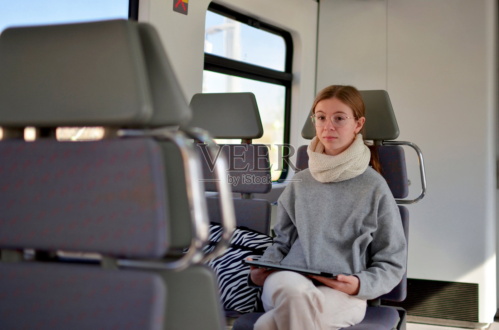 一个戴眼镜的女孩坐在火车上，手里拿着一台平板电脑。照片摄影图片