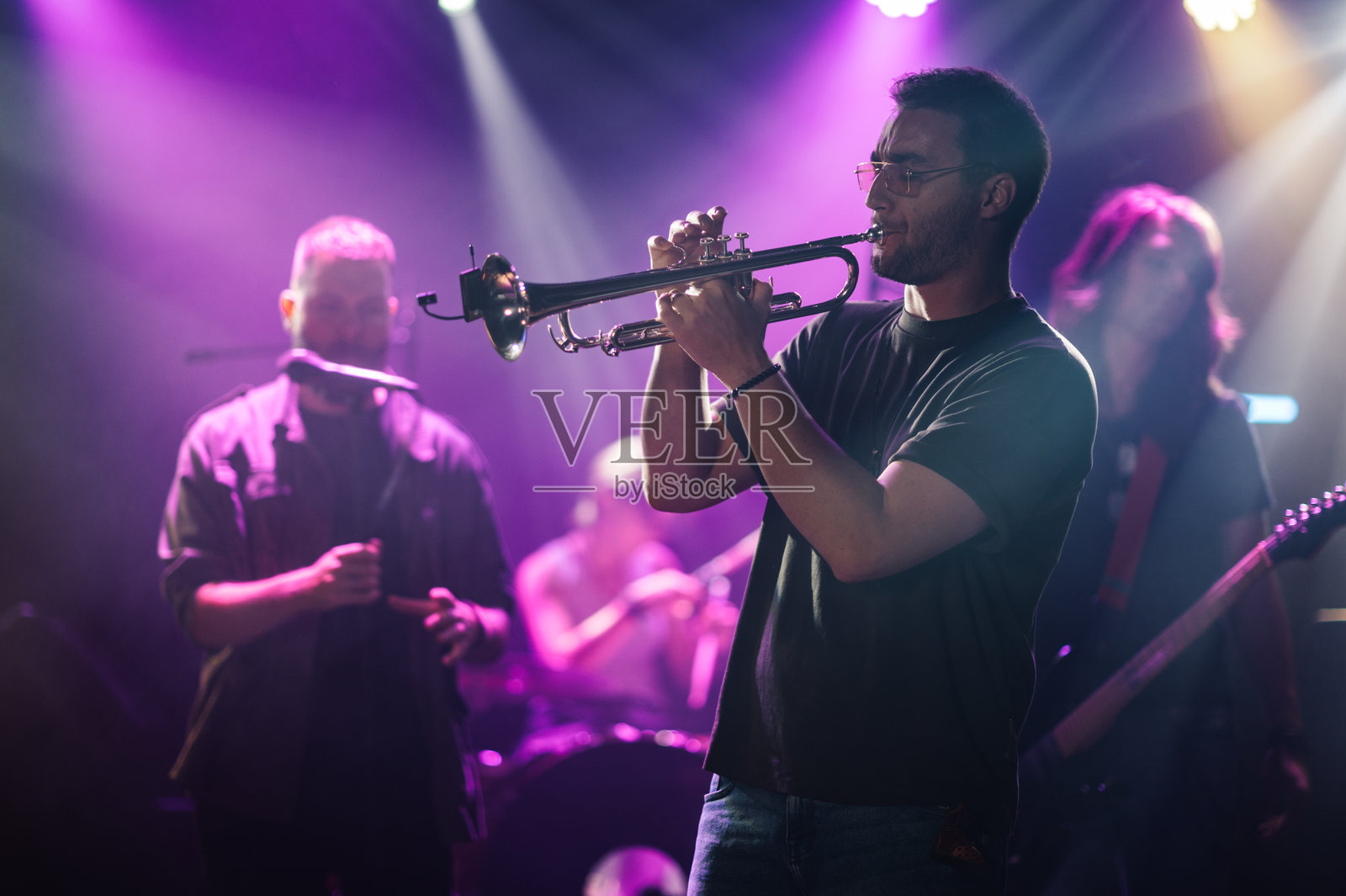 在紫色灯光下与乐队一起现场演奏的小号手照片摄影图片