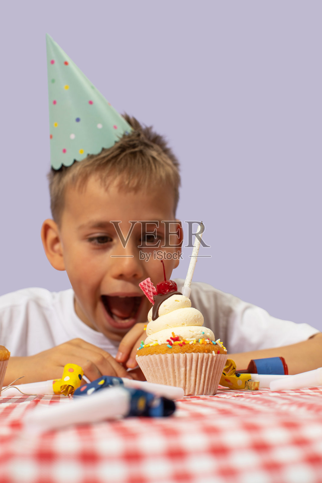 微笑的男孩伸手去咬生日杯子蛋糕上的蜡烛照片摄影图片