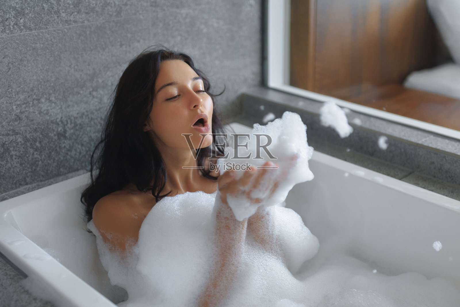 女人在奢华环境中享受放松的泡泡浴，吹出泡沫照片摄影图片