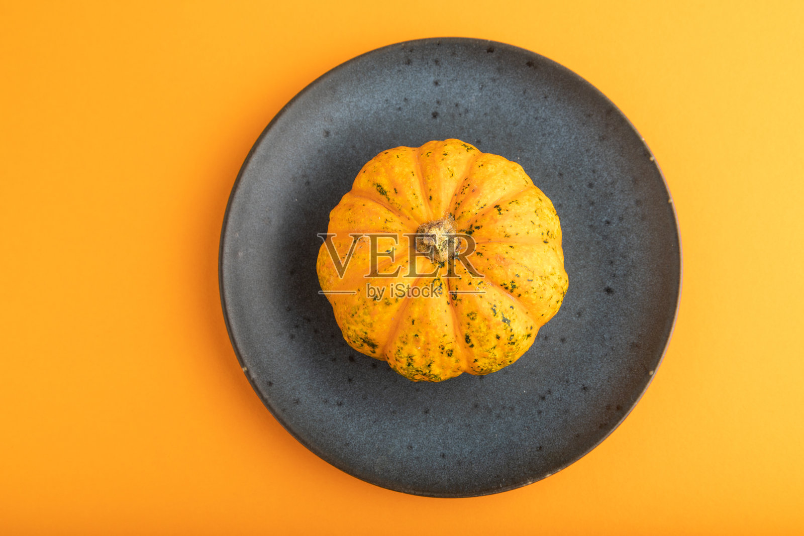 蓝色盘子上的橙色南瓜，放在橙色粉彩纸上。俯视图，留白空间。照片摄影图片