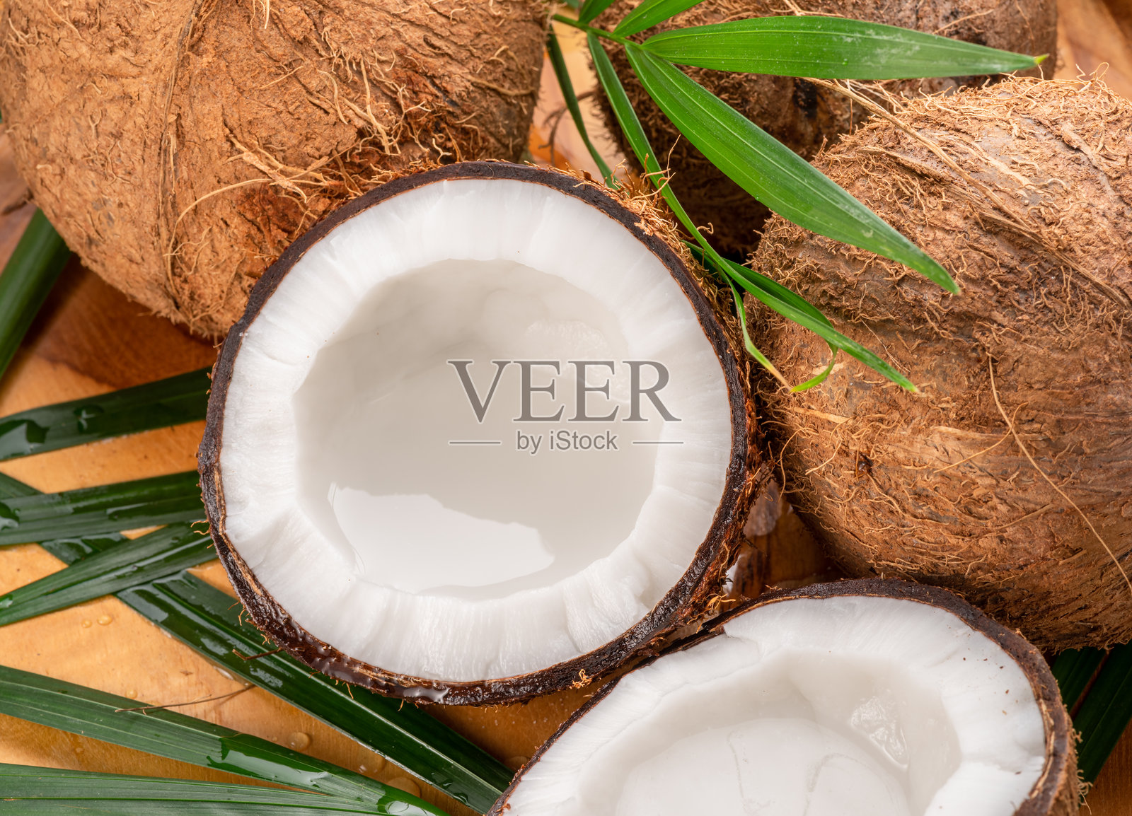 新鲜打开的椰子、完整的椰子和椰子叶放在木桌上。为您的项目提供美丽的热带水果背景。照片摄影图片