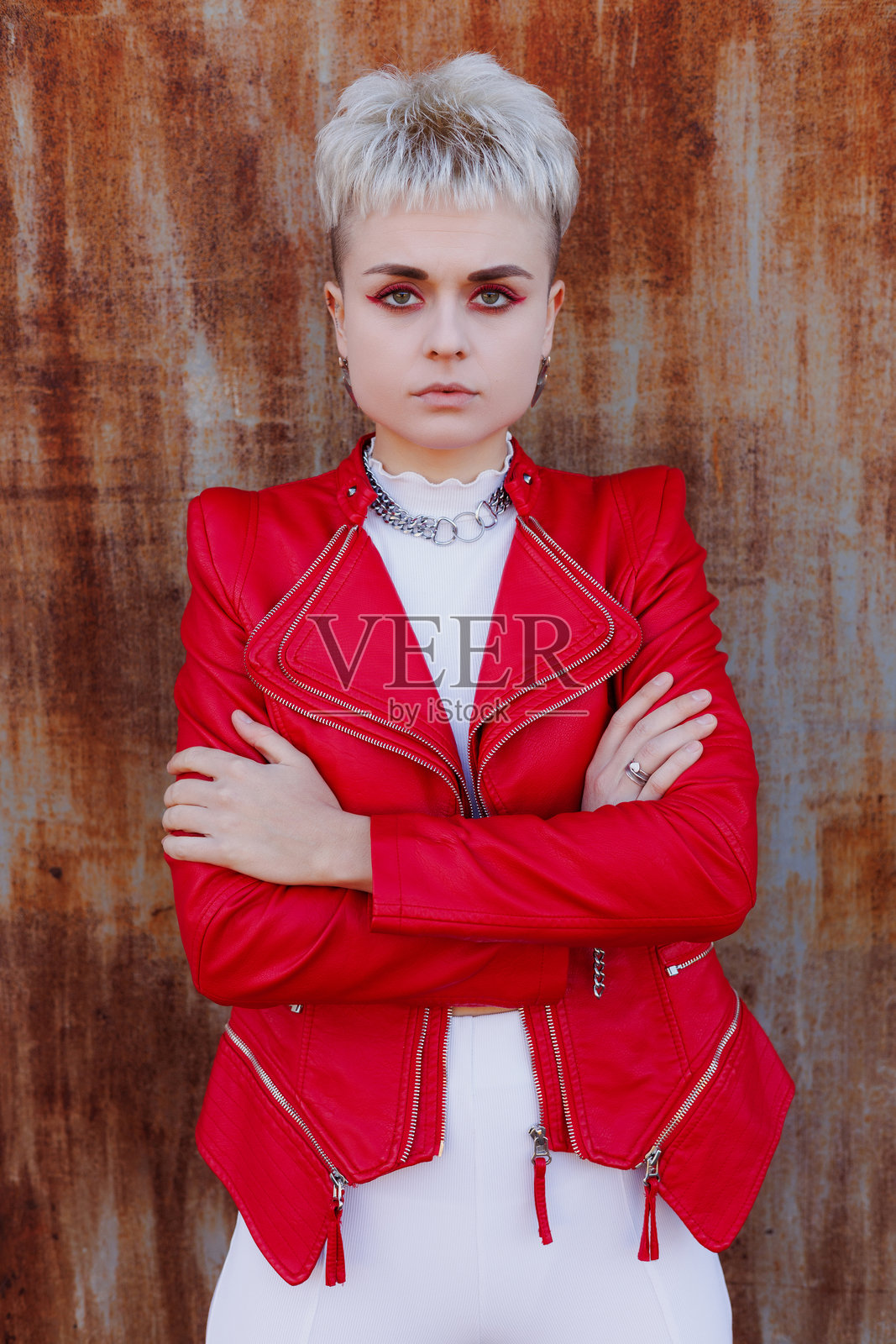 自信的现代女性穿着亮色皮夹克，面对镜头，背景为有纹理的生锈表面。照片摄影图片