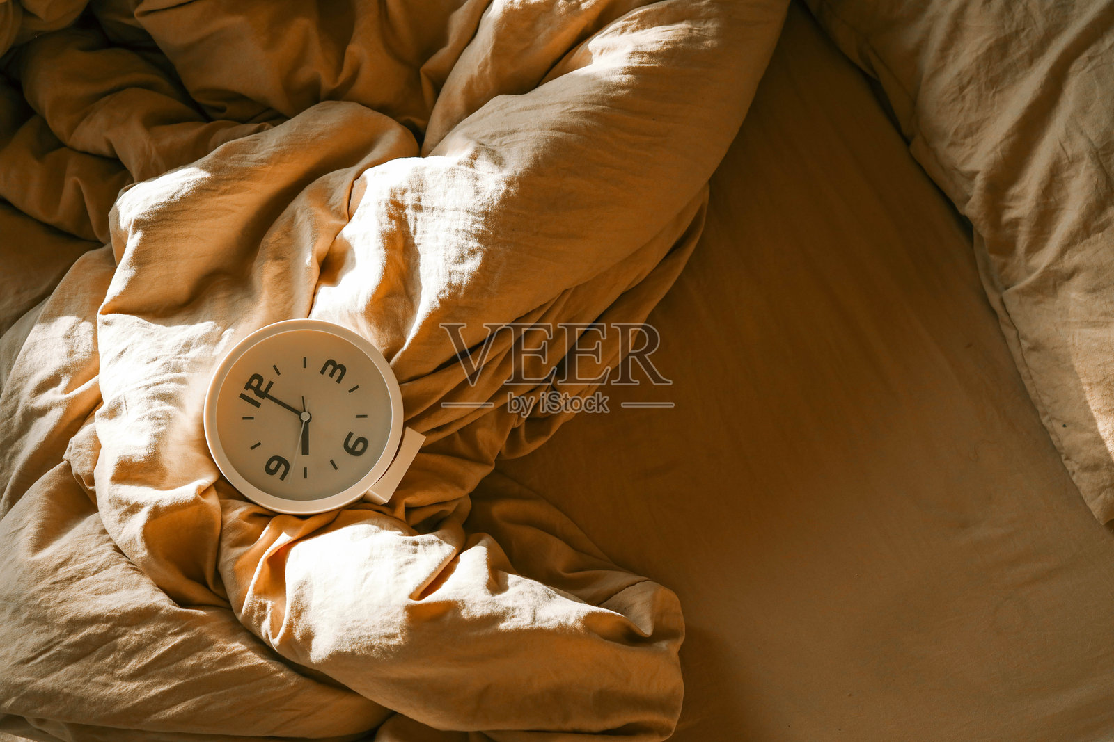 一个白色的闹钟放在柔软的米色毛毯上，营造出一种温馨和清晨觉醒的氛围。照片摄影图片