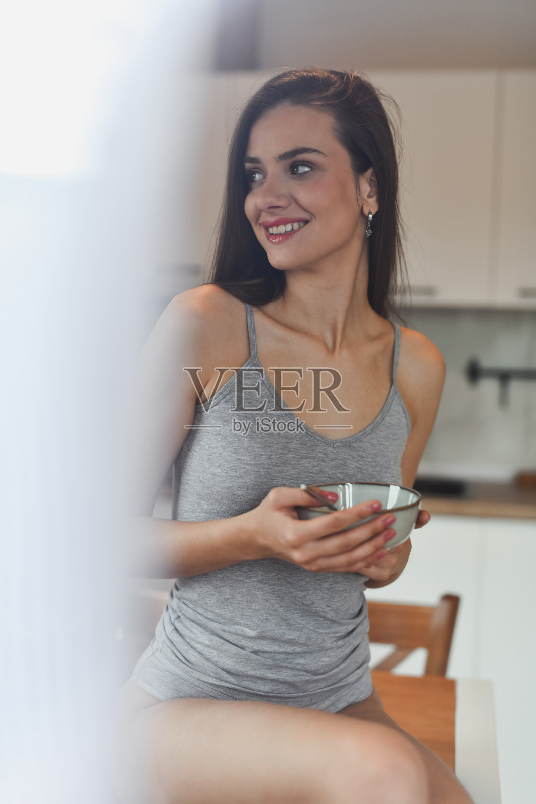 微笑的女性坐在餐桌上，穿着灰色内衣，享受温暖的早餐照片摄影图片