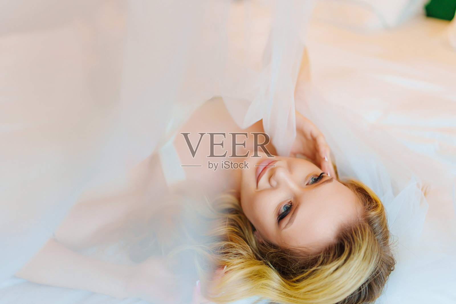 新娘的早晨。娇嫩美丽的金发新娘在床上，面纱轻覆。照片摄影图片