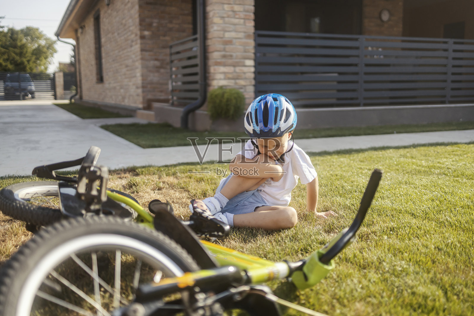 哭泣的小男孩在后院从自行车上摔倒，正捂着受伤的膝盖。照片摄影图片