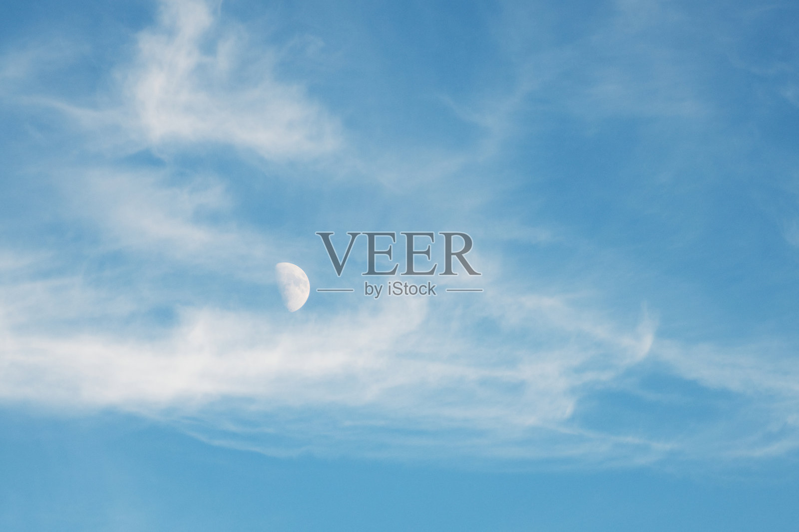 在这张白天的图片中，第一季度的月亮似乎与云朵一起漂浮。照片摄影图片