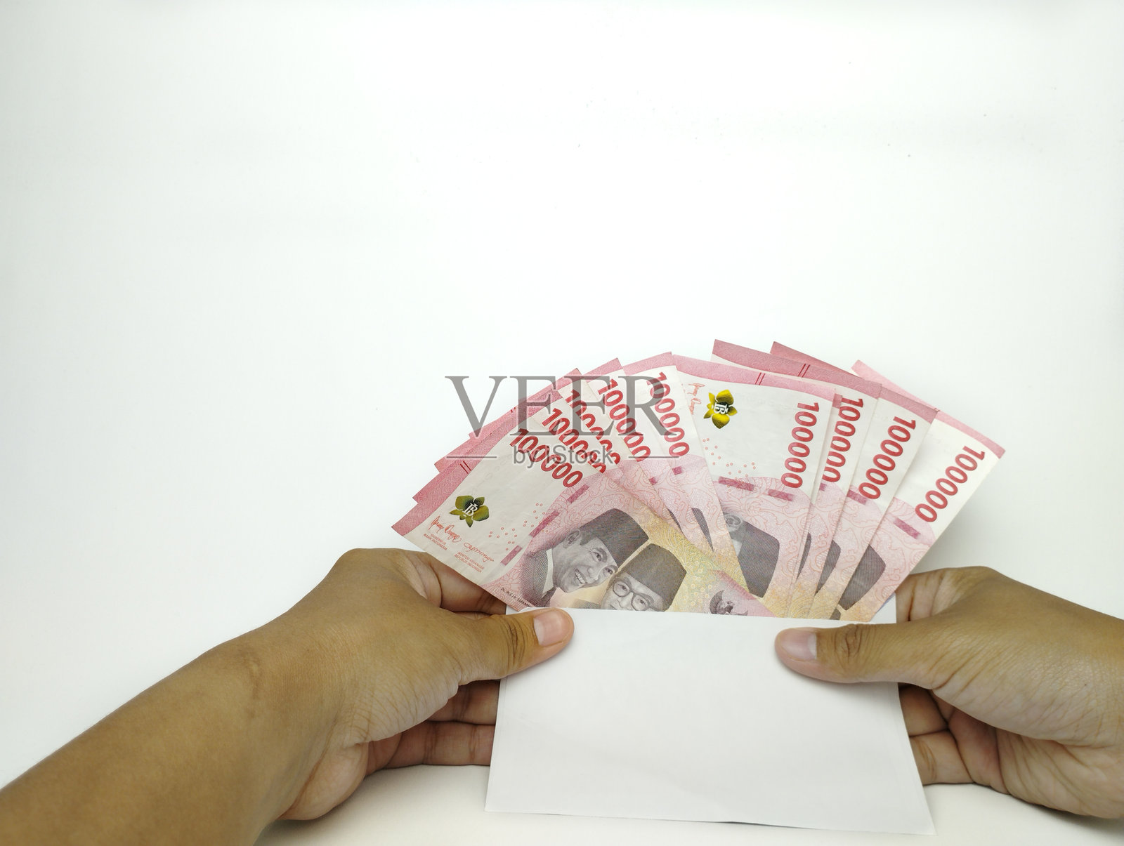 一只手握着十万印尼钞票。现金支付概念。印尼卢比货币（Rp. 100,000 一百卢比）在白色背景上。照片摄影图片
