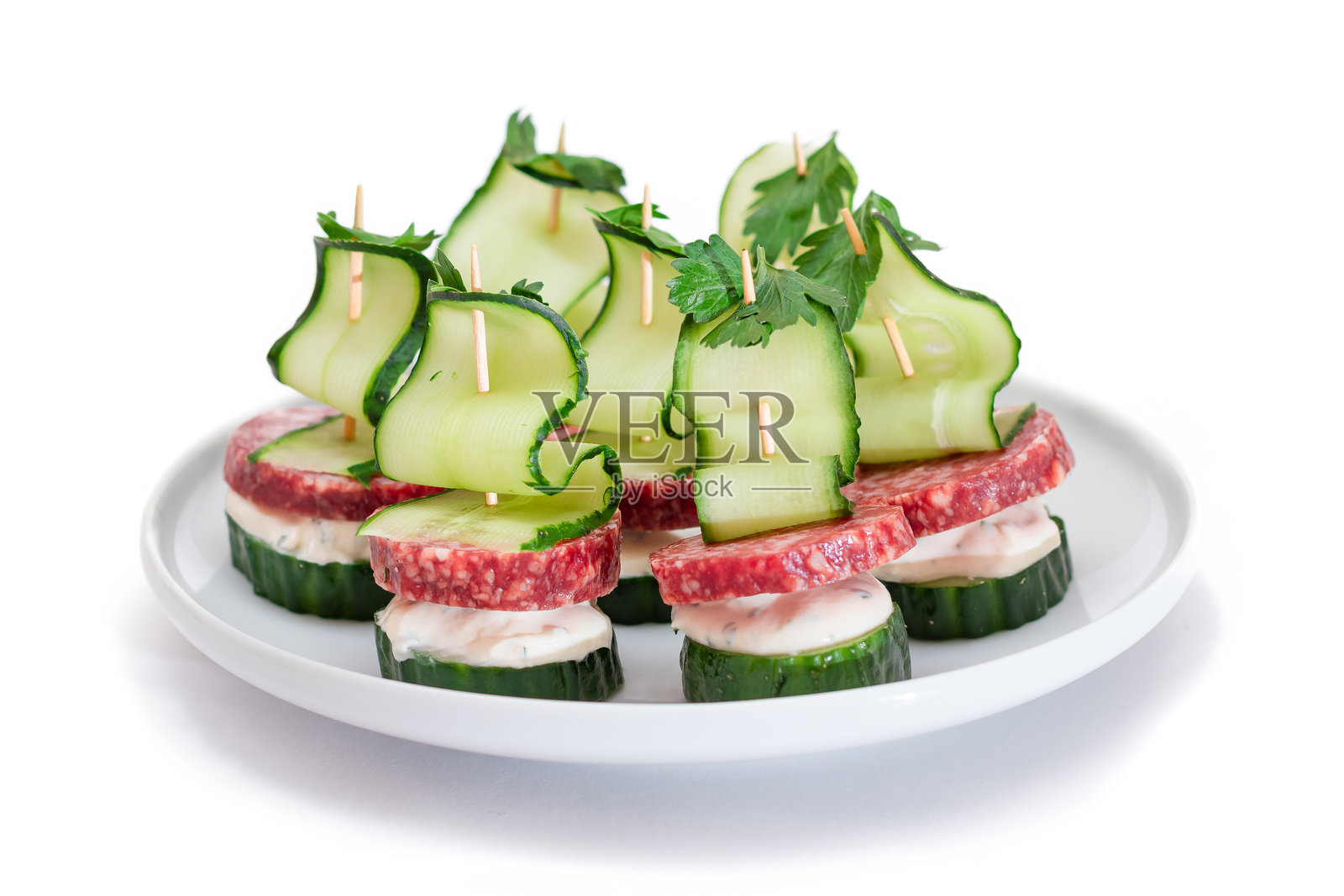 无面包的开胃小菜，配有香肠、黄瓜、绿叶蔬菜和奶油奶酪，摆放在白色盘子上照片摄影图片