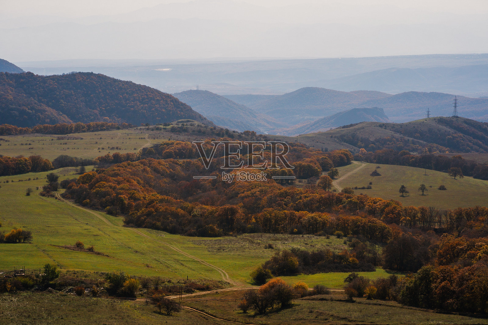 广袤的秋季风景，展现起伏的山丘和五彩斑斓的树叶，在正午的朦胧天空下。照片摄影图片