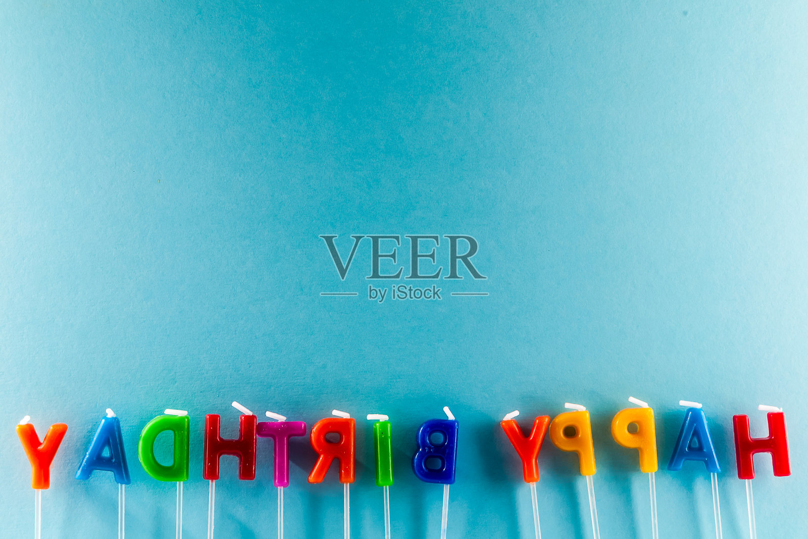 蓝色背景上排成一行的五彩蜡烛拼写着“生日快乐”照片摄影图片