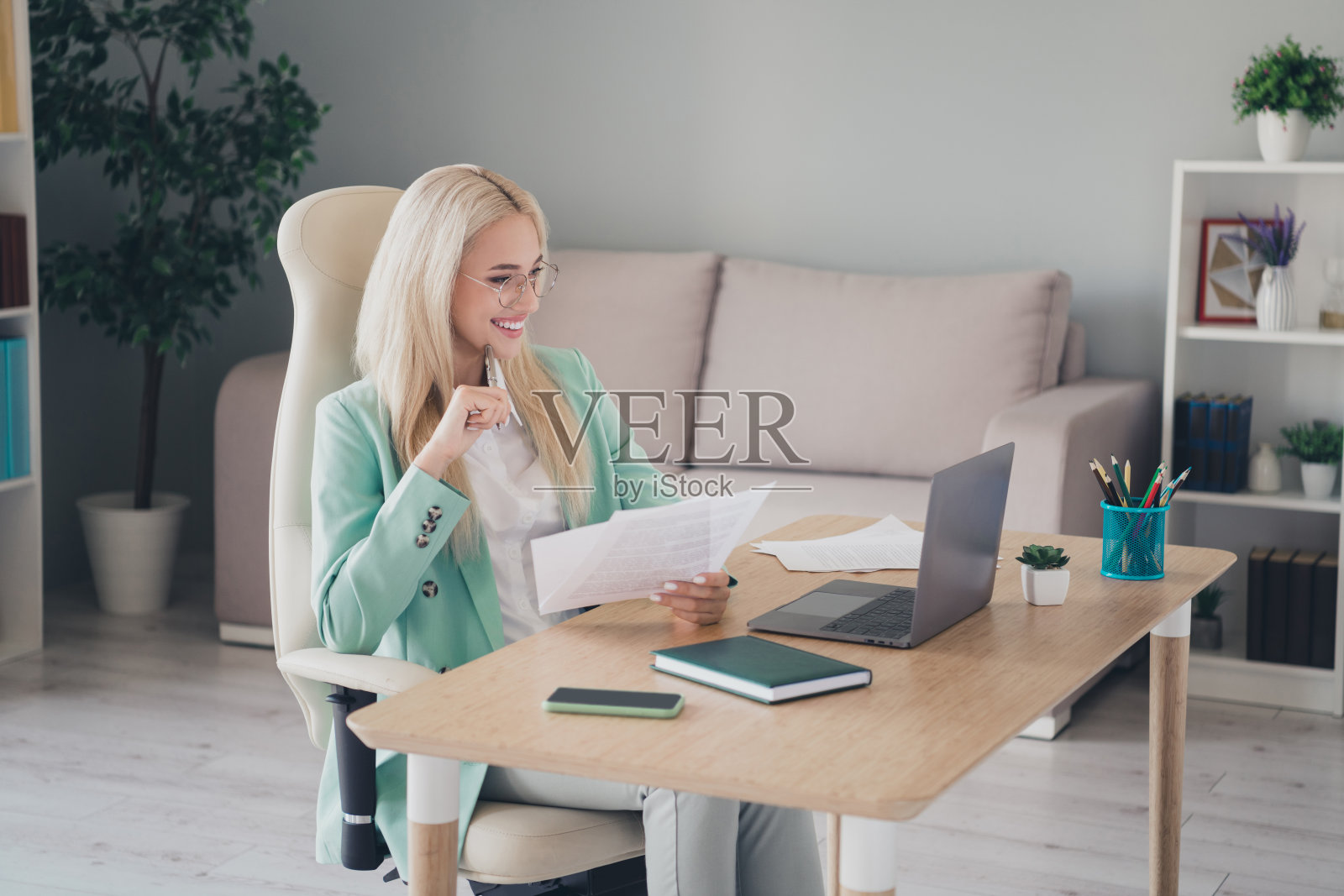 心情愉快的漂亮女性穿着青色西装，在室内工作站阅读现代设备的文件照片摄影图片