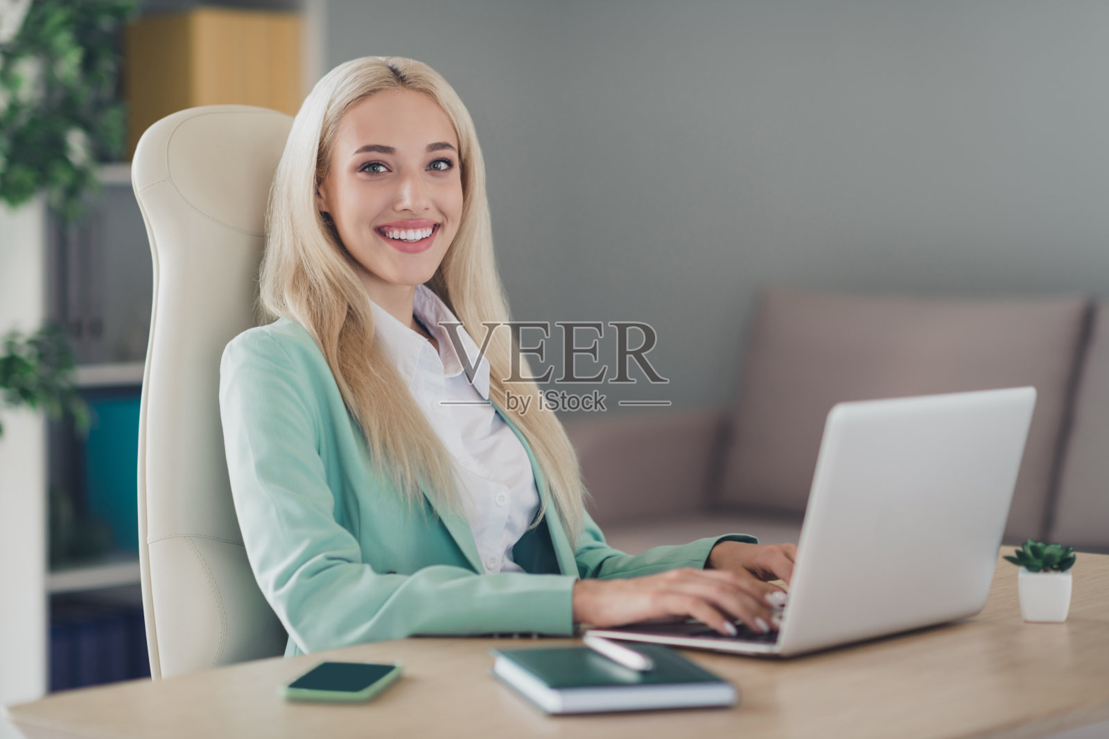 一位愉快迷人的女士坐在椅子上，使用无线笔记本电脑打邮件，进行室内工作网络交流。照片摄影图片