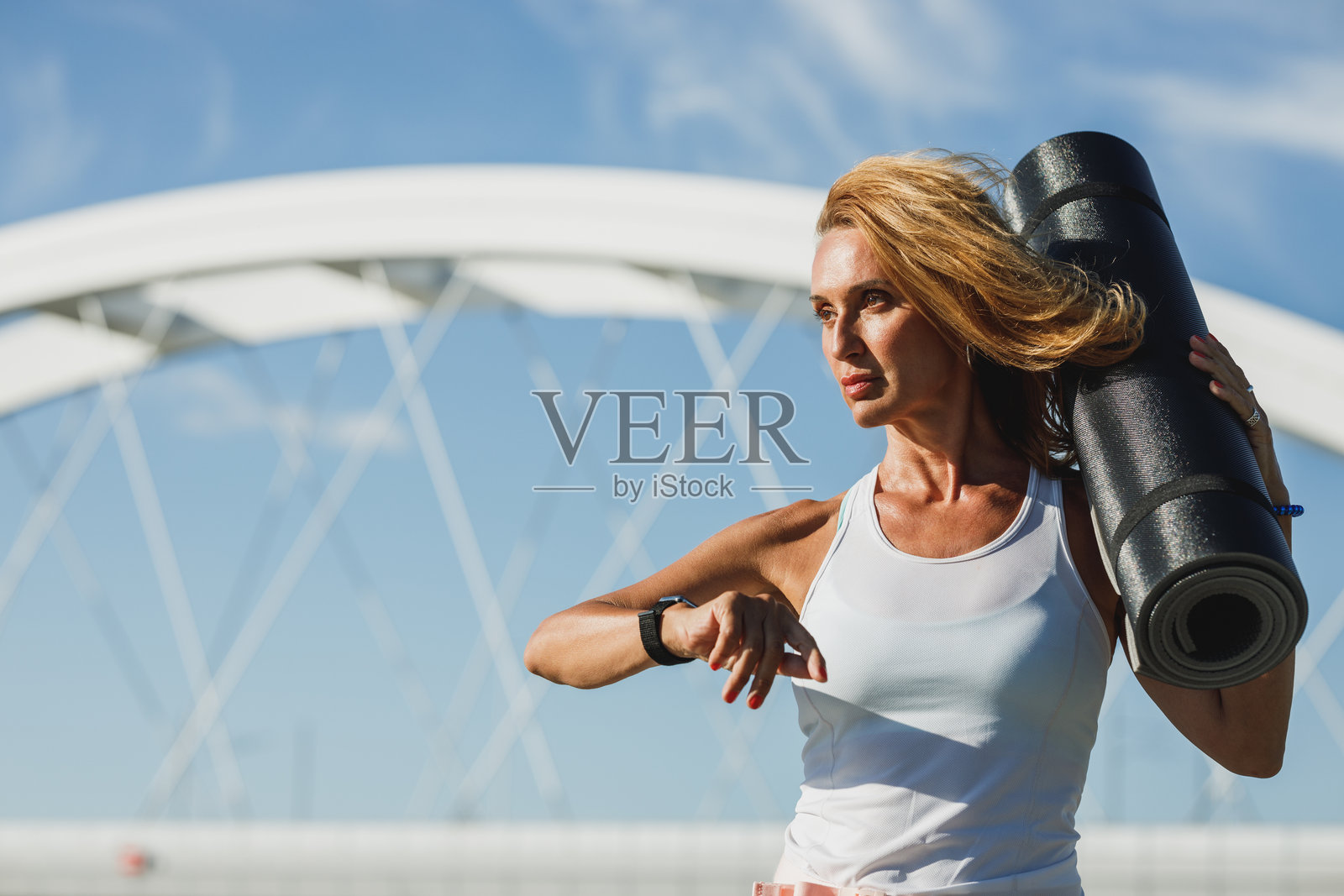 佩戴智能手表的女性手持卷起的瑜伽垫照片摄影图片