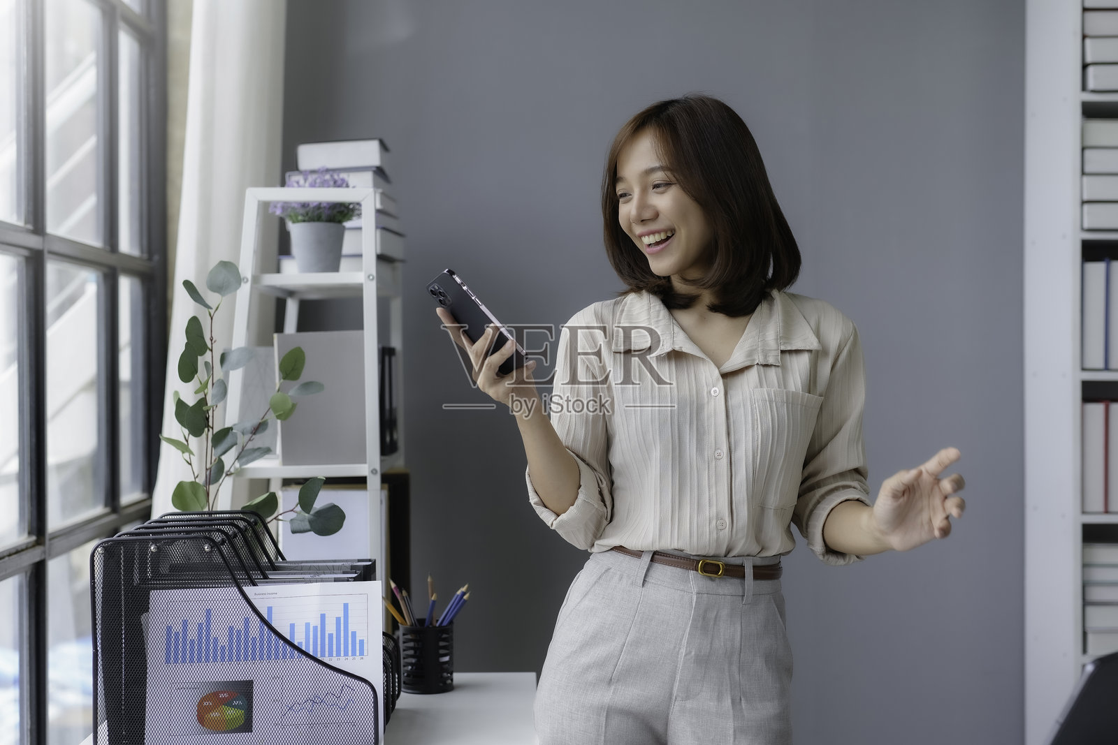 年轻女商人在办公室使用智能手机，微笑并做手势进行视频通话。照片摄影图片