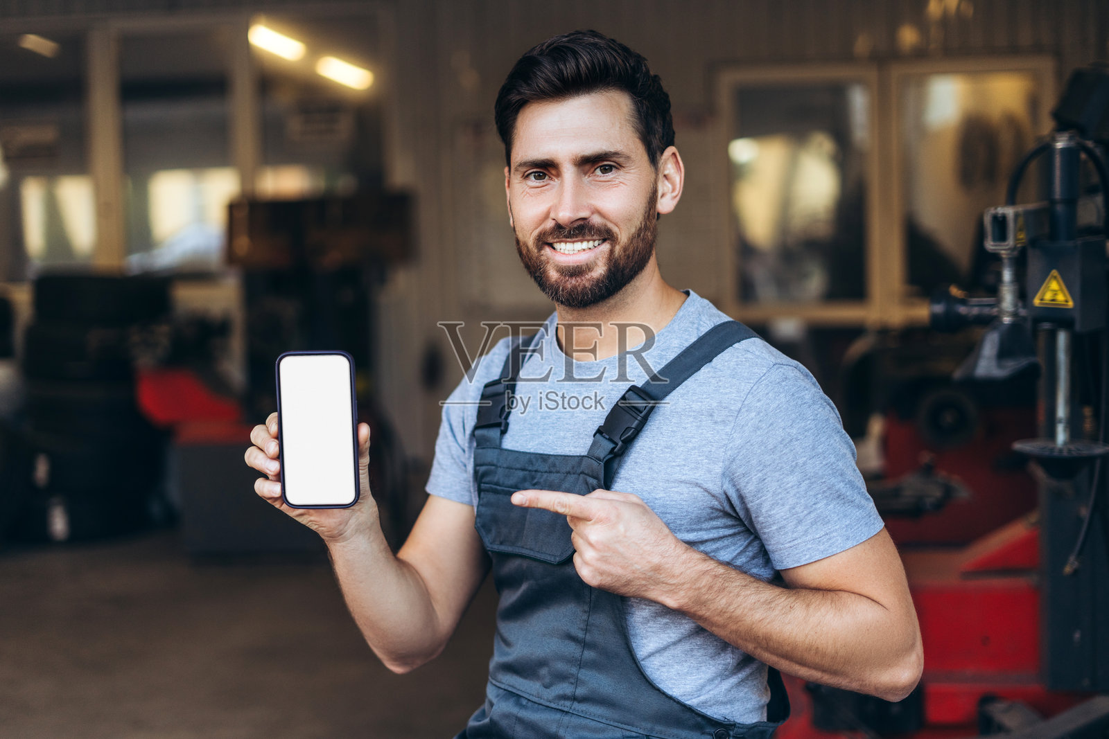 微笑的英俊自信男子，专业修理工，手持一部空白屏幕的智能手机照片摄影图片