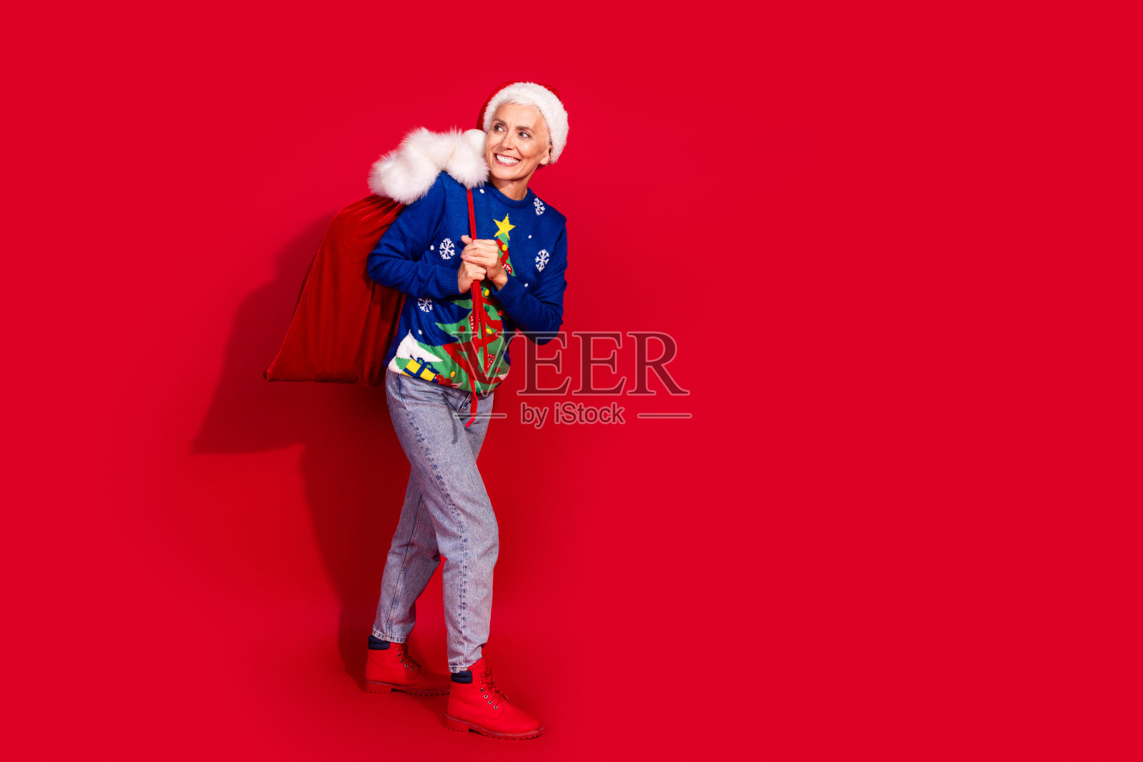 全身肖像的美丽老年女士展示了空袋走路的造型，背景是鲜艳的红色，适合新年和圣诞节的氛围。照片摄影图片