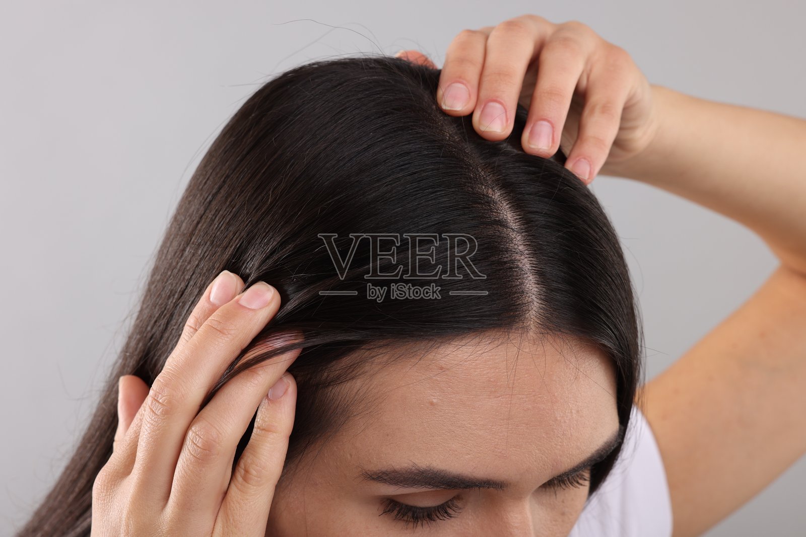 女性在灰色背景下仔细检查自己的头发和头皮，特写镜头照片摄影图片
