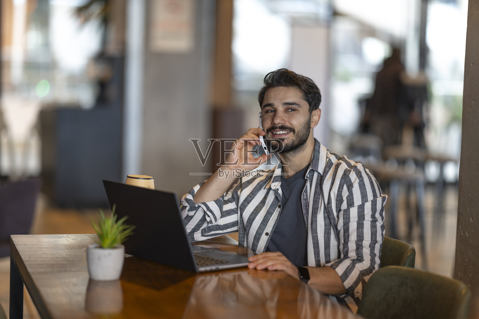 年轻的商人在咖啡馆里一边打电话一边使用笔记本电脑工作照片摄影图片