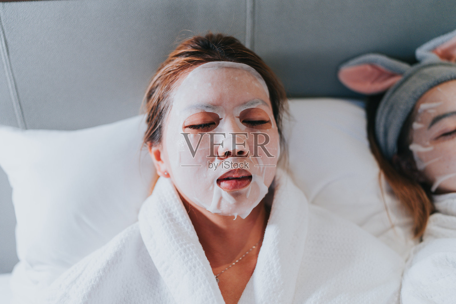 快乐的Z世代女孩们在中国大湾区珠海旅行。她们脸上戴着面膜，正在酒店房间的床上休息。照片摄影图片