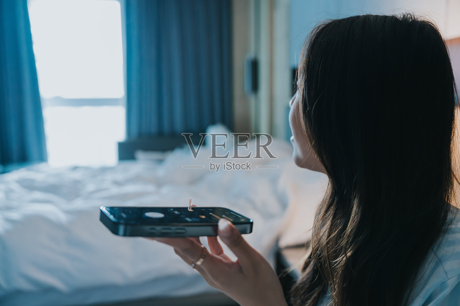 亚洲女孩在房间里使用智能家居技术，通过手机应用的语音识别功能打开窗帘。照片摄影图片