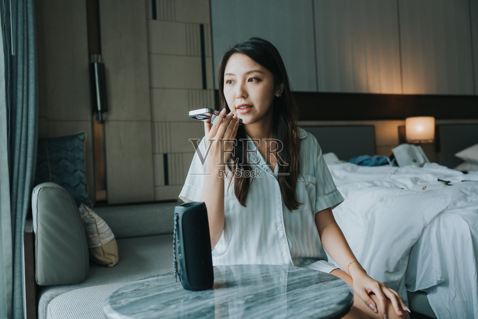 亚洲女孩在房间里使用带语音识别的智能家居技术，通过扬声器和手机应用进行操作。照片摄影图片