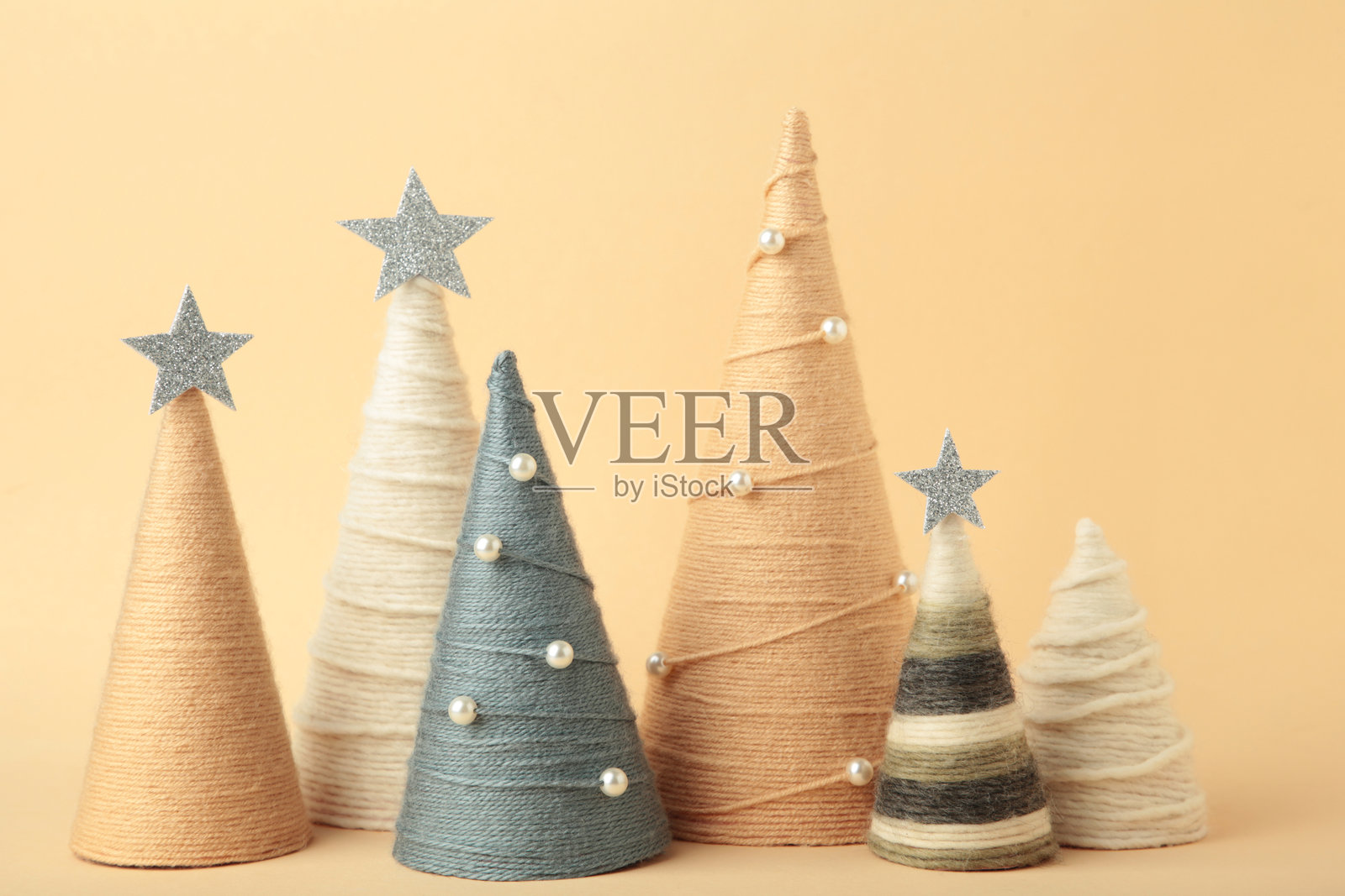 手工制作的圣诞树，背景为米色。用毛线包裹的锥形树。DIY概念照片摄影图片