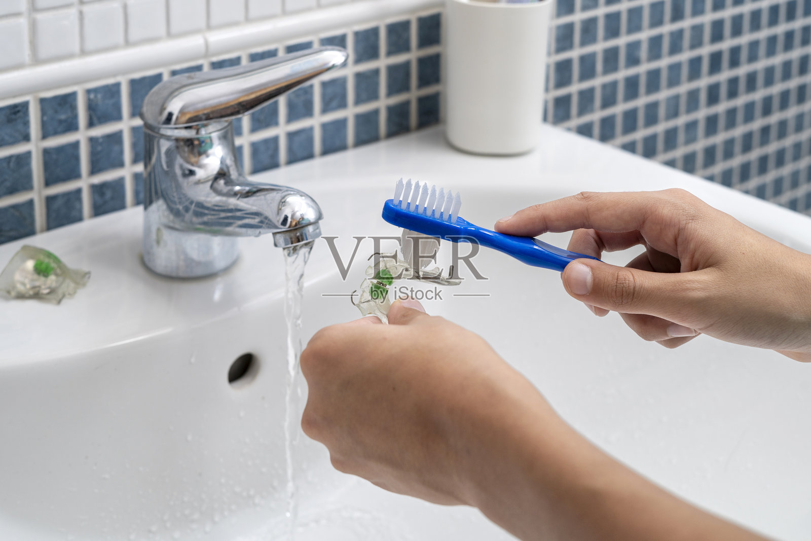 在流动的自来水下清洗牙齿矫正器的手照片摄影图片