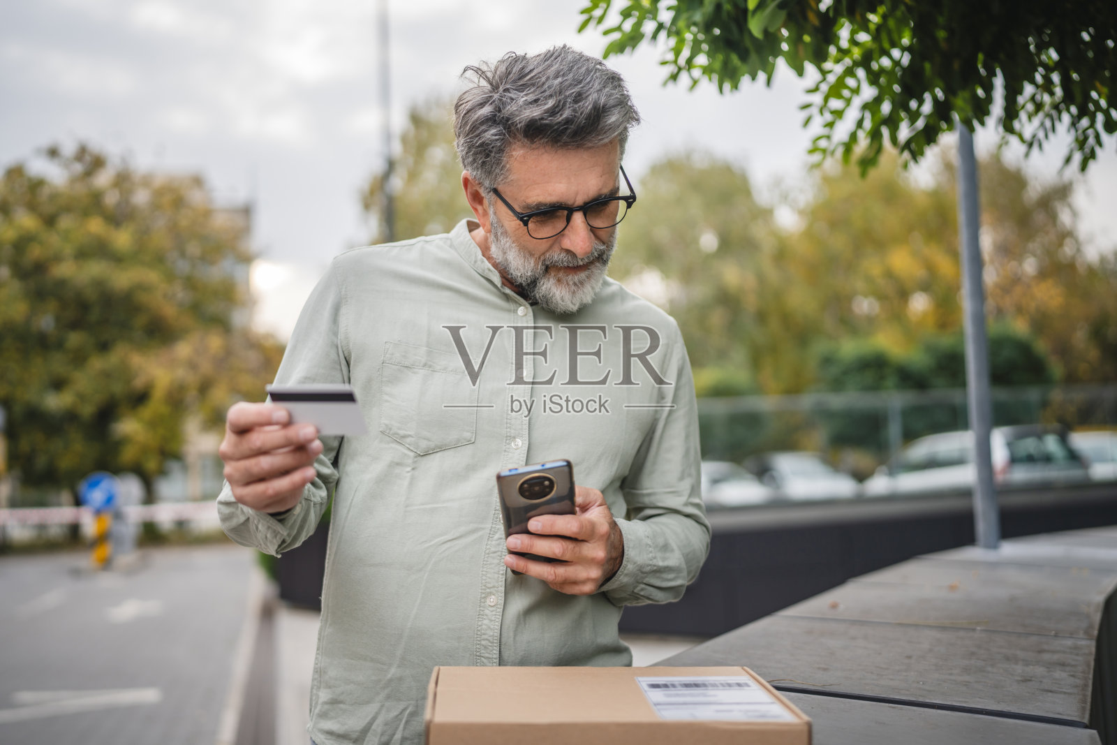 老年男子在户外手持信用卡、手机和包裹照片摄影图片