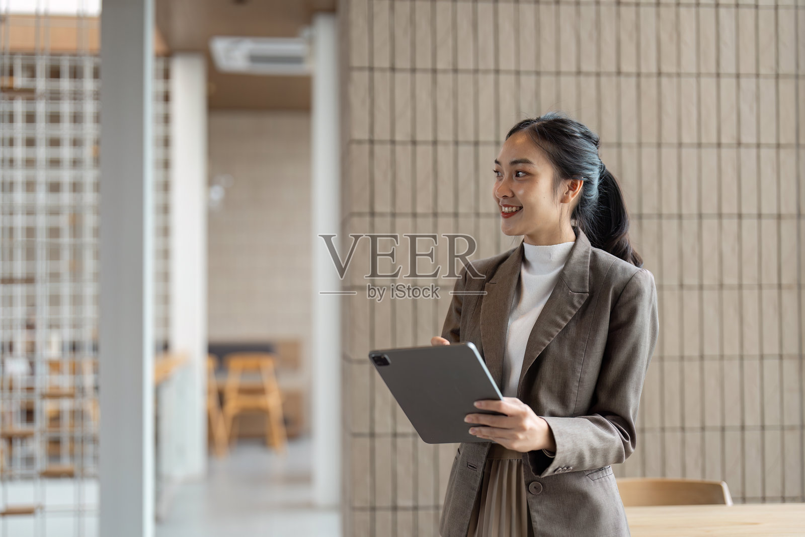 自信的女商人在现代办公室环境中手持平板，象征着职业成功与创新照片摄影图片