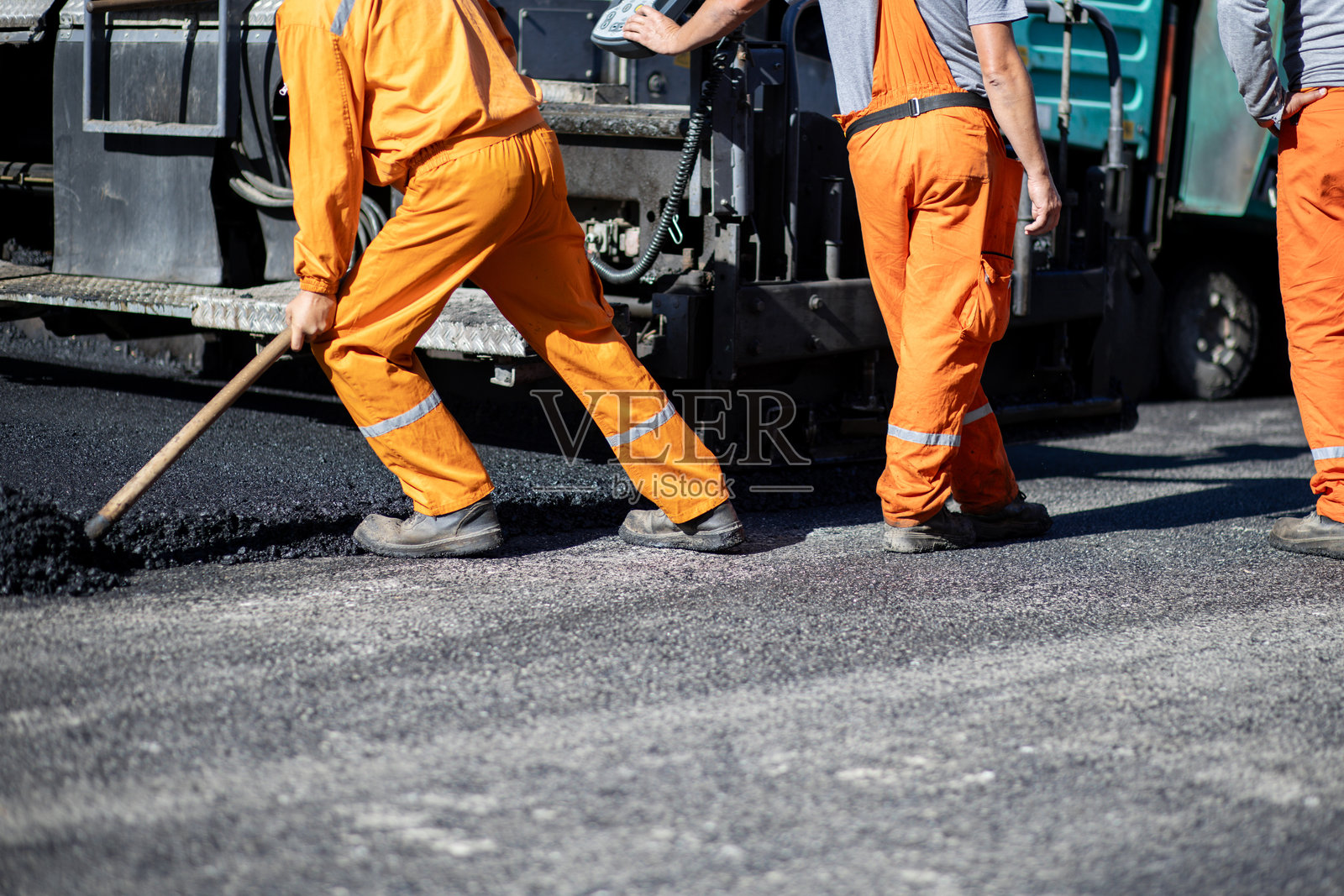 建筑工人在繁忙的城市区域白天穿着亮橙色制服铺设沥青道路照片摄影图片
